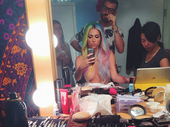 Kesha fazendo selfie no espelho, com cabelões coloridos e sem sutiã.